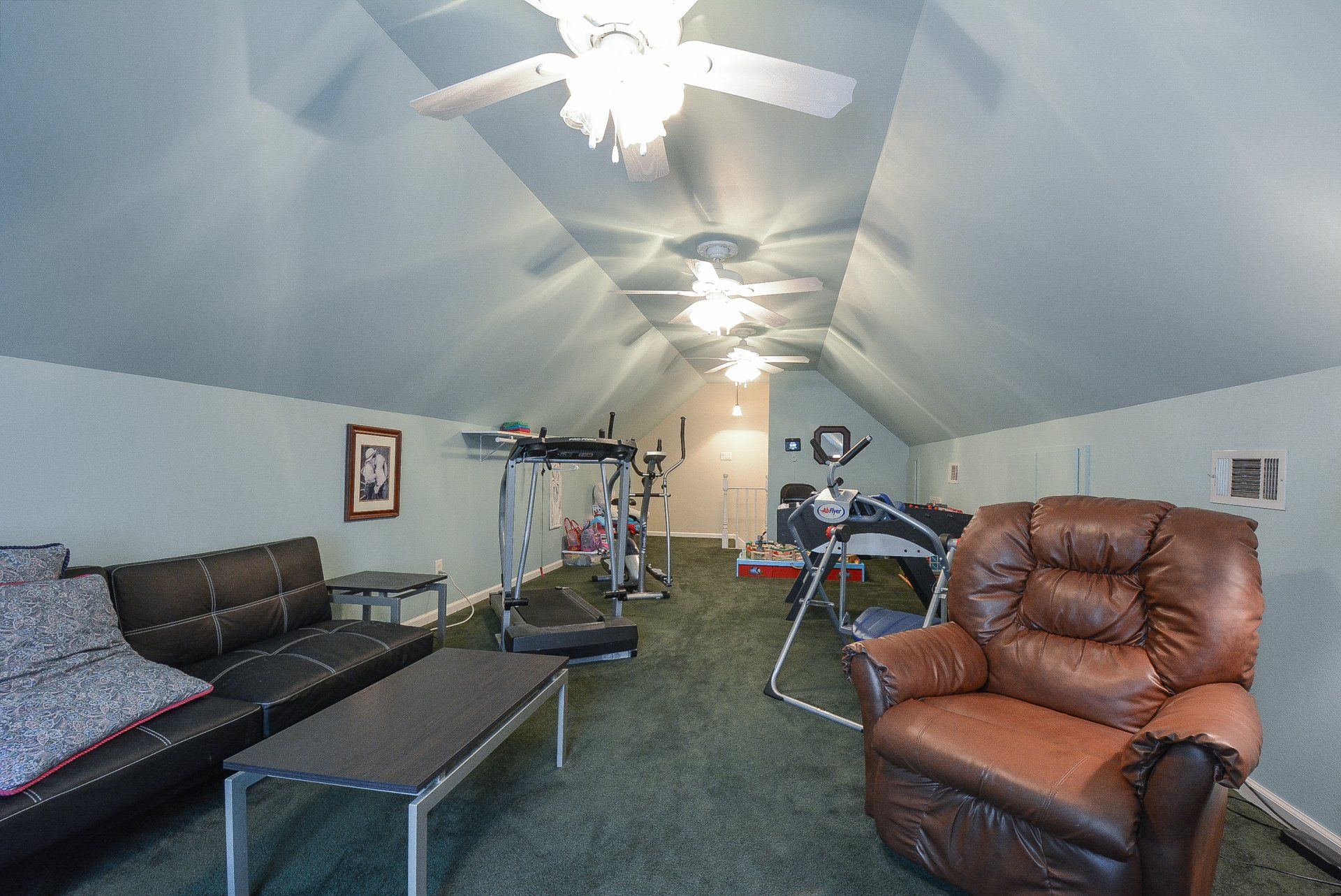 Room with a couch, exercise equipment, and a recliner chair under a sloped ceiling.