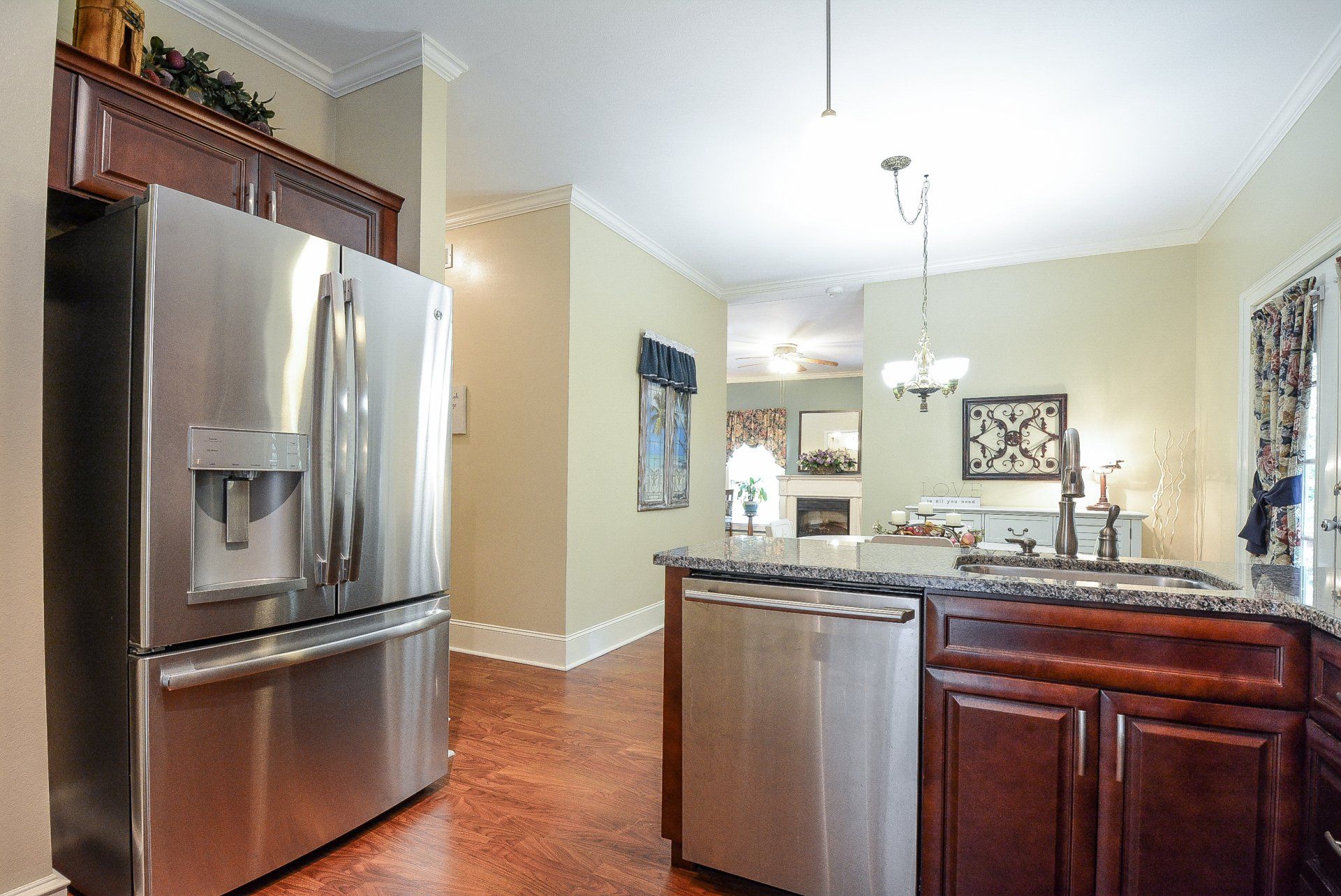 Stainless steel kitchen with refrigerator, dishwasher, and dark wood cabinets, leading to living room.