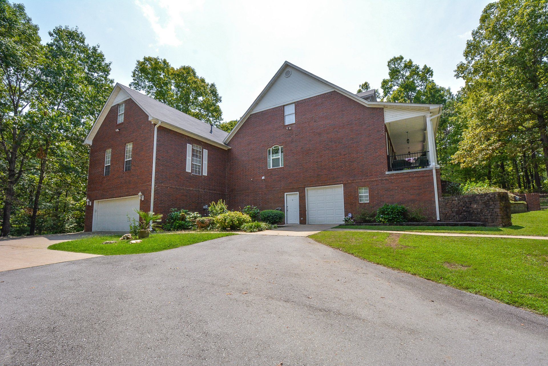 Brick house with a driveway, two garage doors, and a covered porch surrounded by trees.