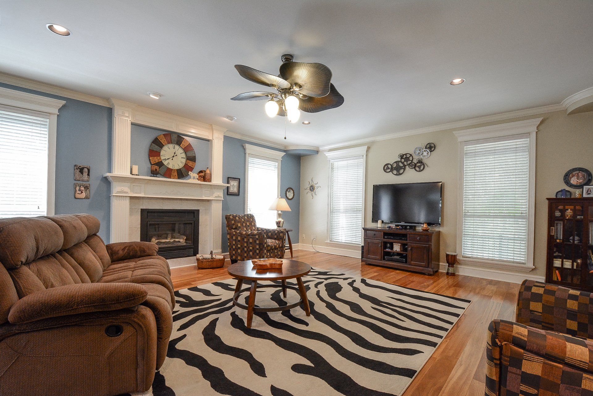 Living room with zebra rug, fireplace, brown furniture, and television.