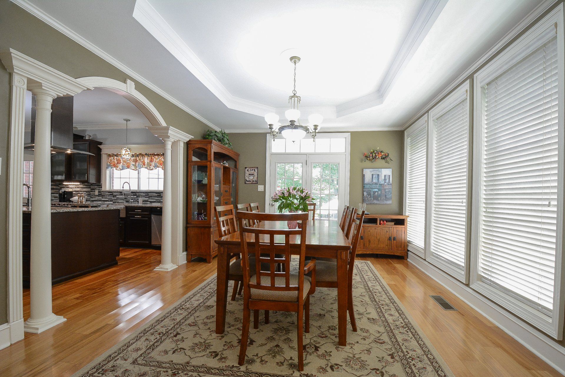Dining room with wood table, chairs, rug, and view to kitchen, light streaming from windows.