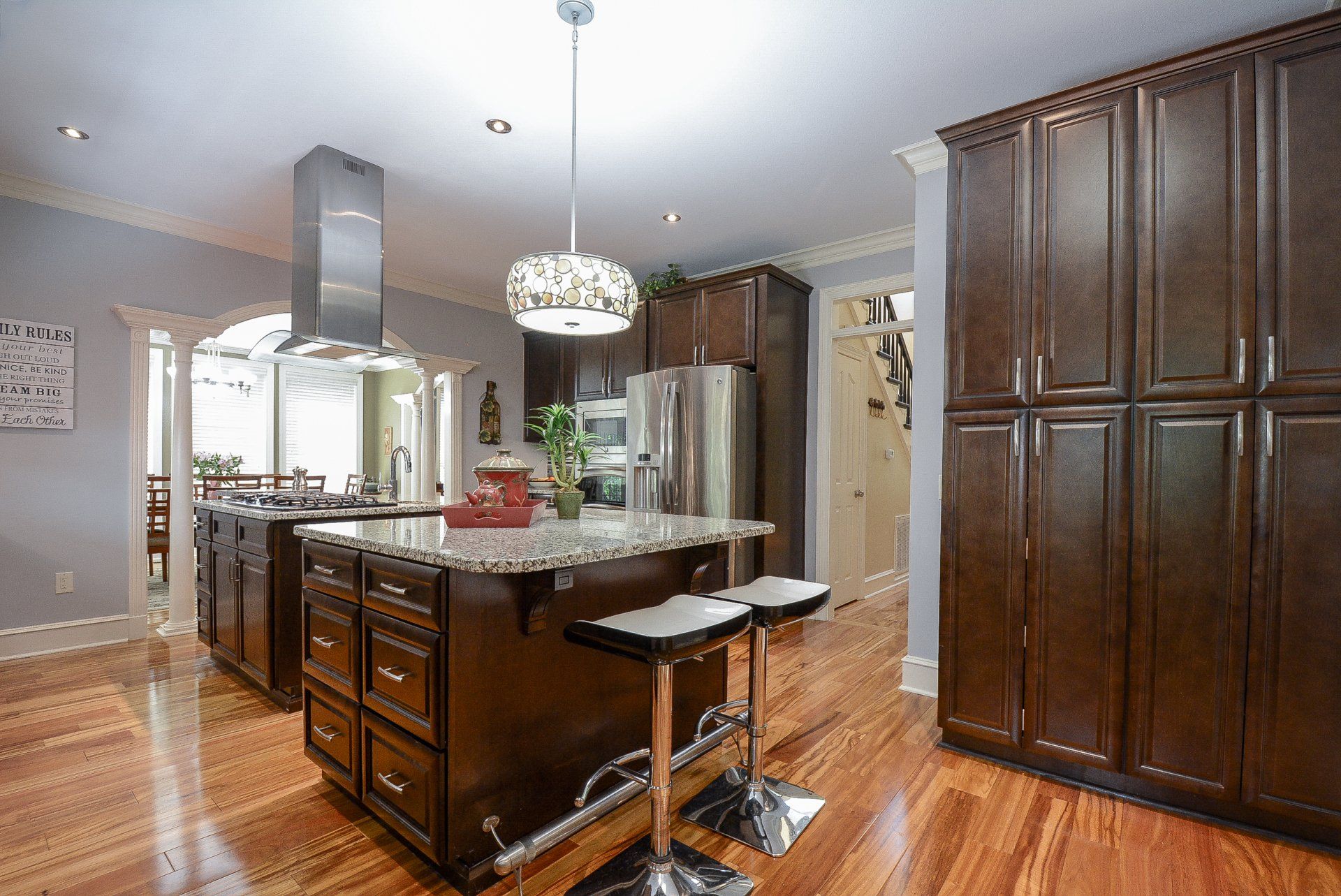 Kitchen with dark brown cabinets, island with seating, stainless steel appliances, hardwood floors.