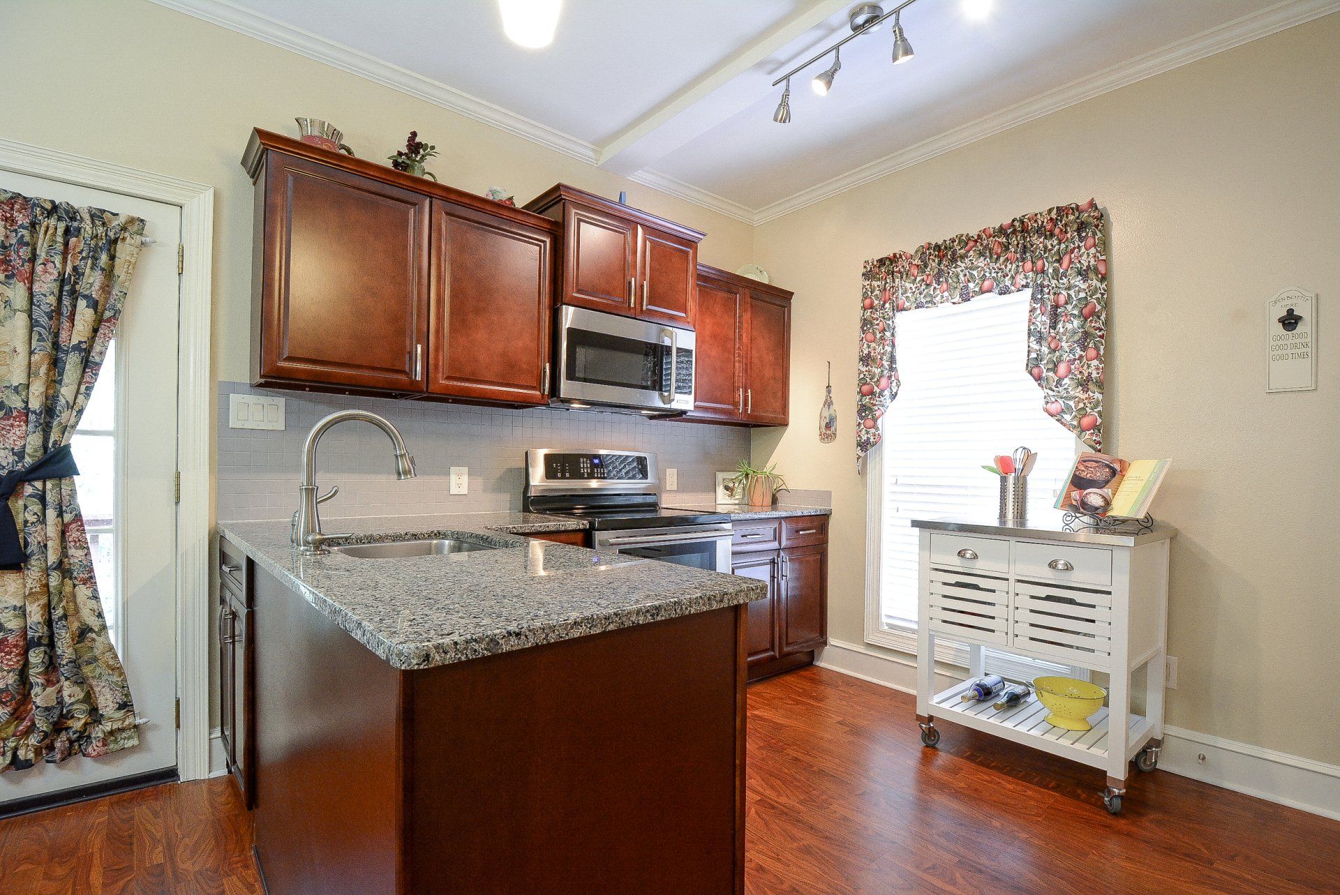 Kitchen with brown cabinets, granite countertop island, stainless steel appliances, and hardwood floor.