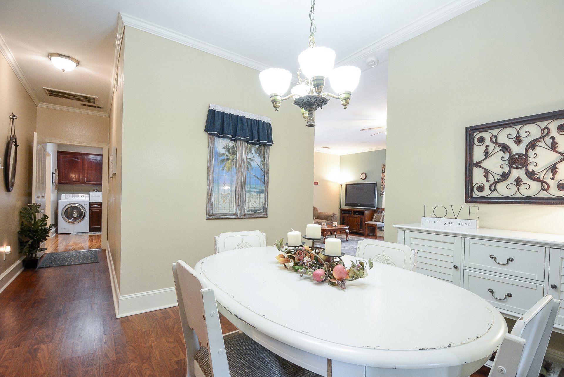 Dining room with oval table, chandelier, white sideboard, and hallway leading to laundry.