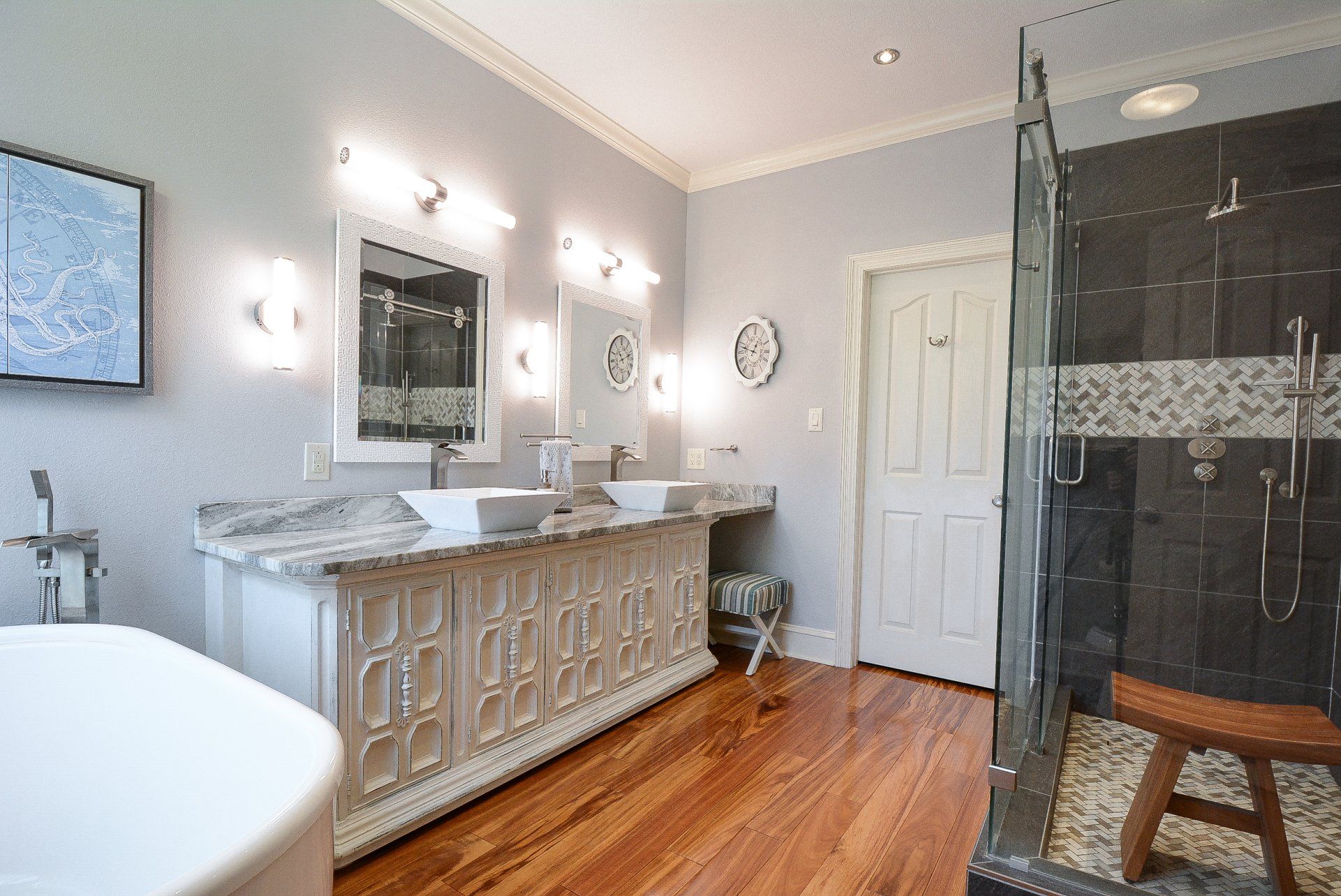 Elegant bathroom with double vanity, white cabinets, and wood floors. Gray walls and large shower.