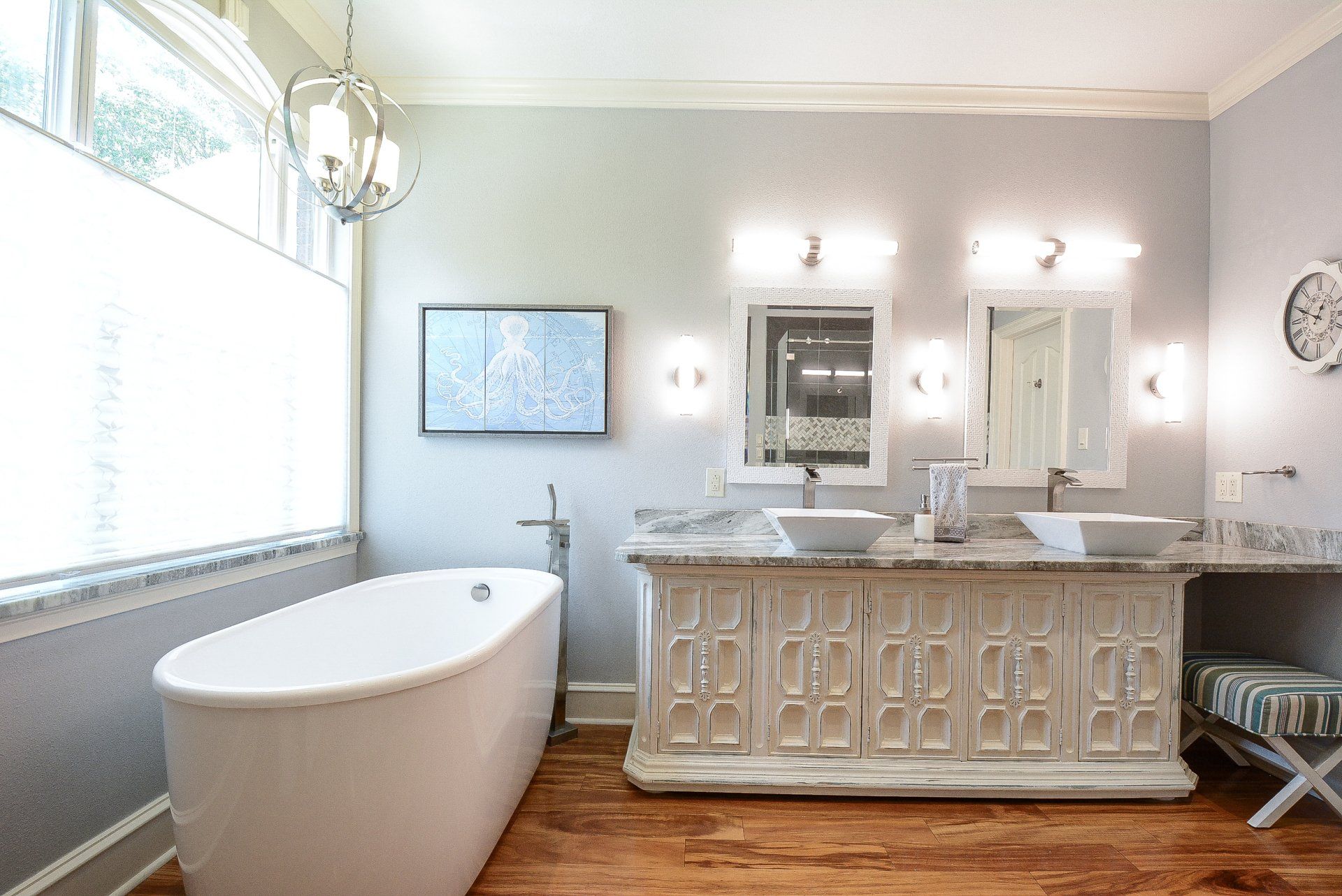 Bathroom with a white tub, double vanity, a TV, and light gray walls.
