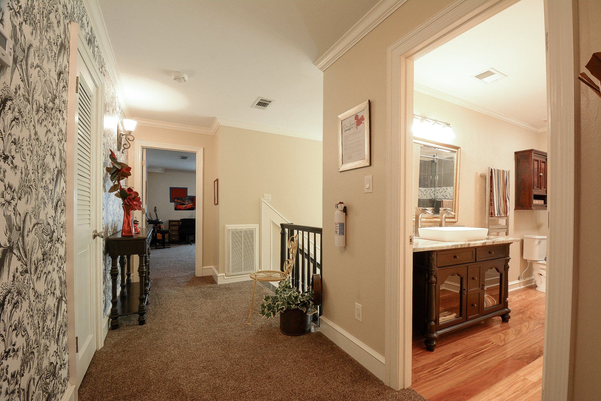 Hallway with floral wallpaper, carpet, and a bathroom doorway with a decorative vanity.