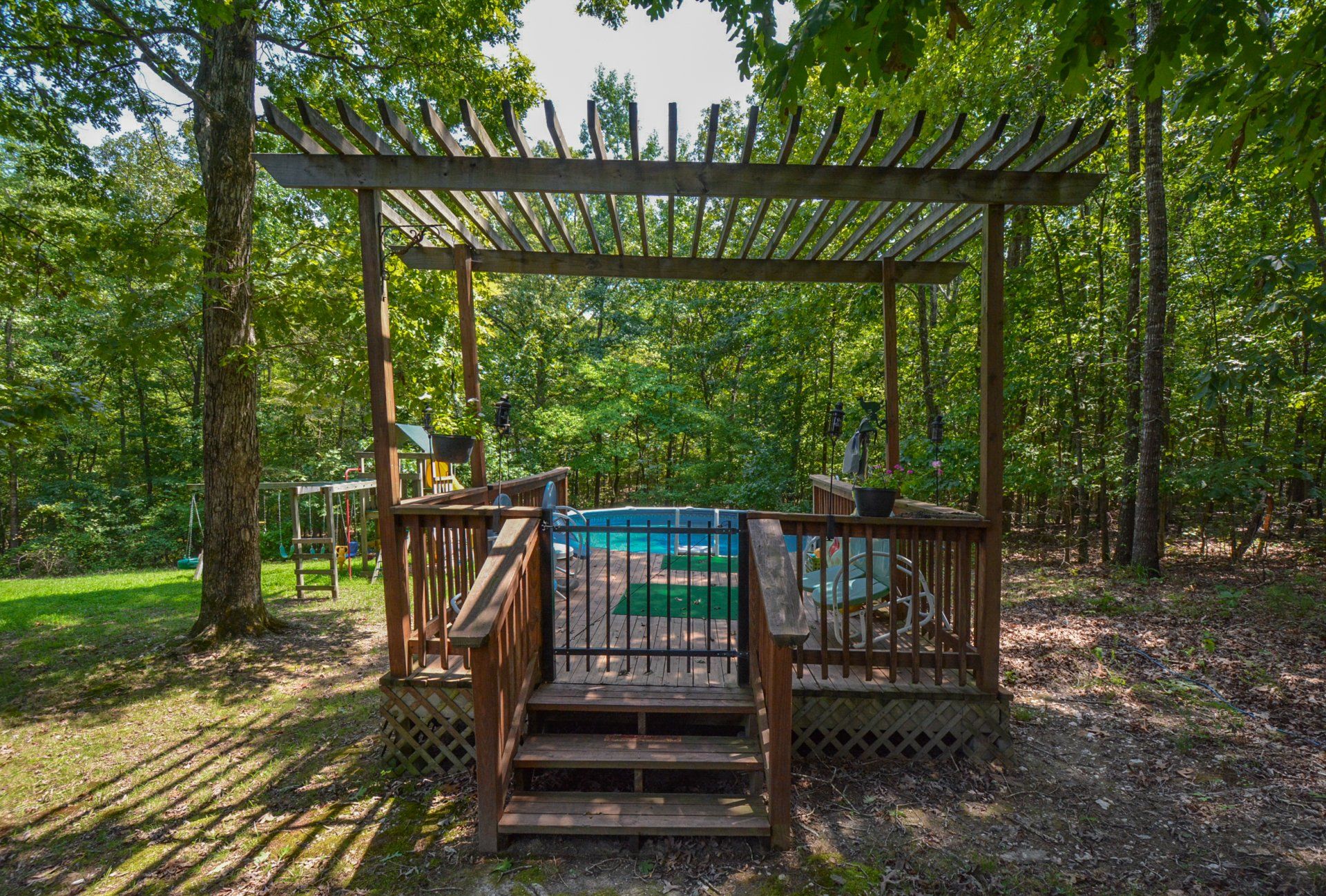 Wooden pergola over a small, blue pool with steps, surrounded by trees.