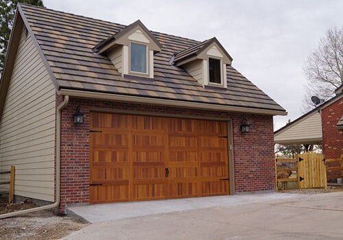 Brick and wood garage with brown door, dormers, and matching roof.
