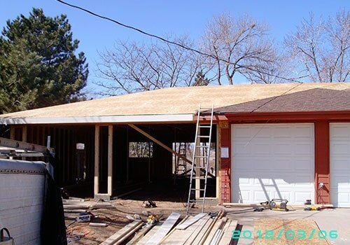 Garage under construction with exposed framing, plywood roof, and ladder.