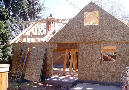 House under construction, wood frame structure, OSB siding, workers on roof, ladder.
