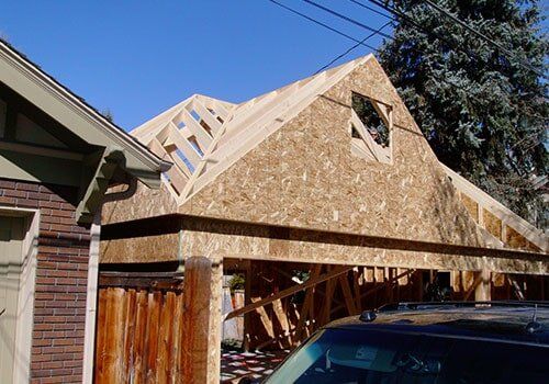 Garage under construction with wooden frame and roof against a blue sky.