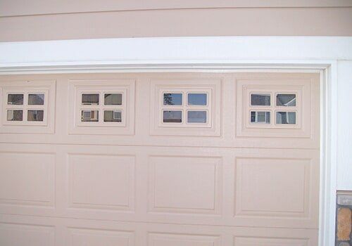 Tan garage door with four square windows at the top.