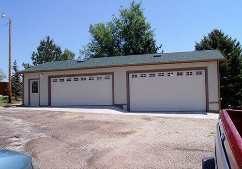 Two-car garage with beige siding and two white garage doors, concrete driveway, and a red pickup truck.