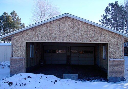 Garage under construction with exposed wood and brick accents, snow in front.