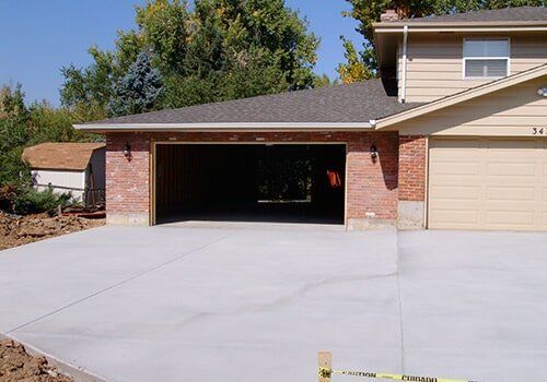 Two-story beige house with red brick garage, open garage door, and concrete driveway.