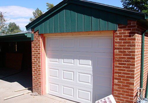 White garage door framed by red brick, green trim above.