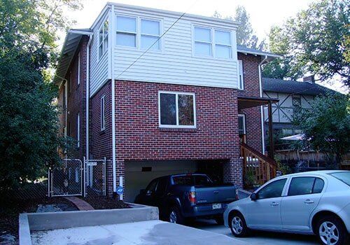 Two-story brick house with a garage holding a truck and car. White upper level and trees surround.