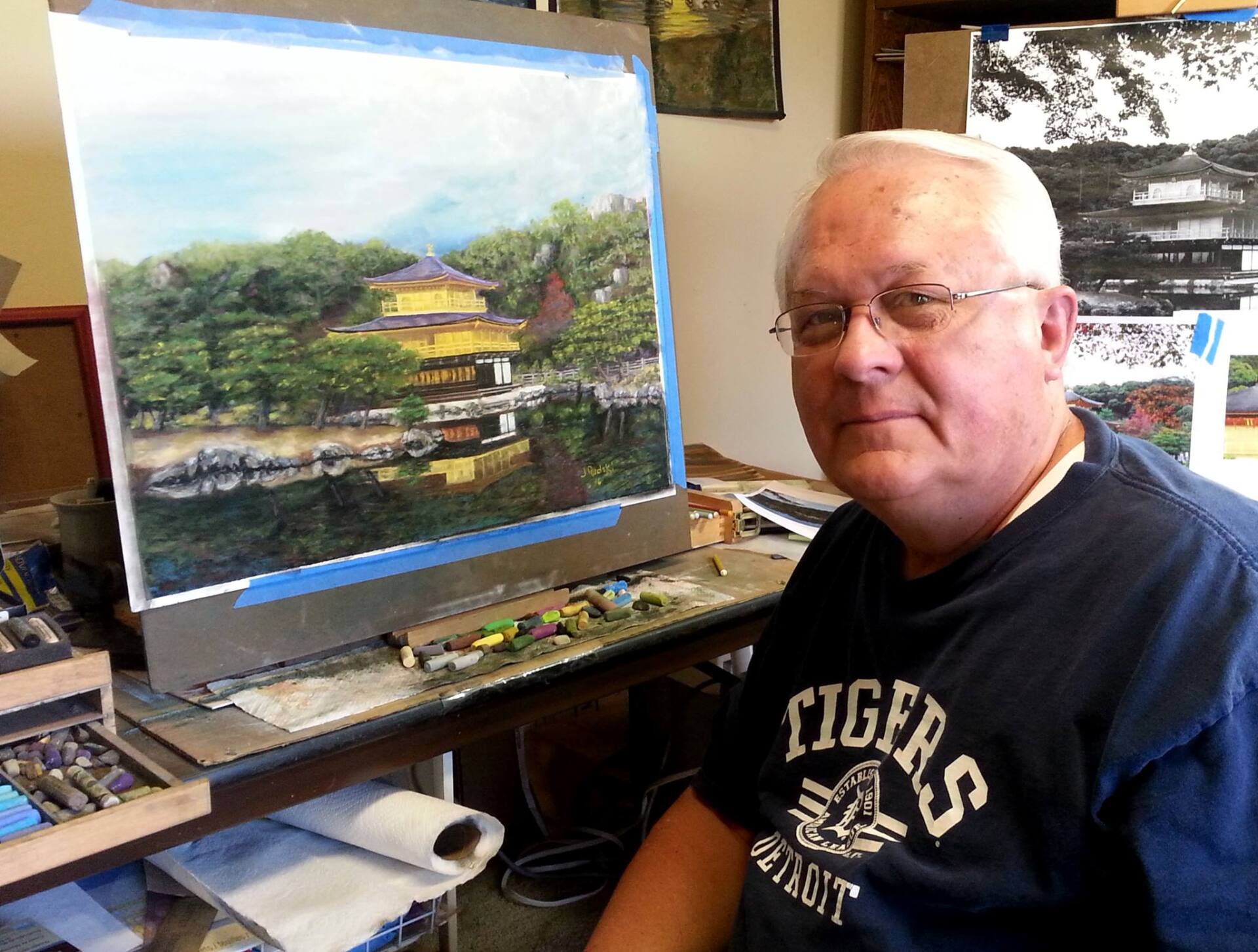 A man wearing a tigers shirt sits in front of a painting