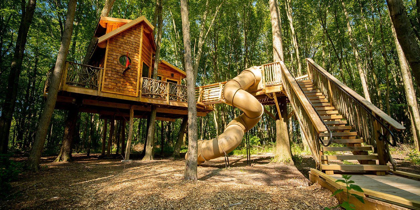 A tree house with a slide and stairs in the woods.