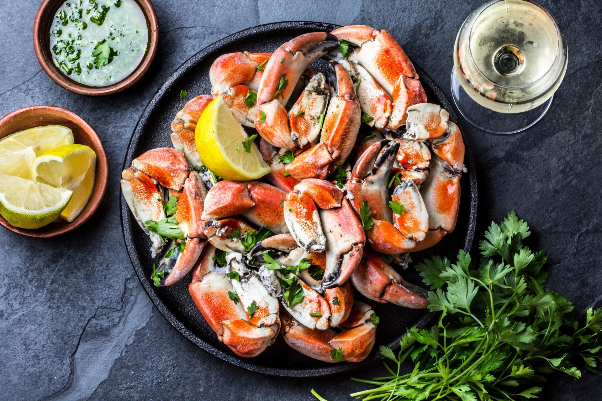 Seafood. Crabs tentacles on black plate with wite wine, lemon and herbs sauce on slate background. Top view.