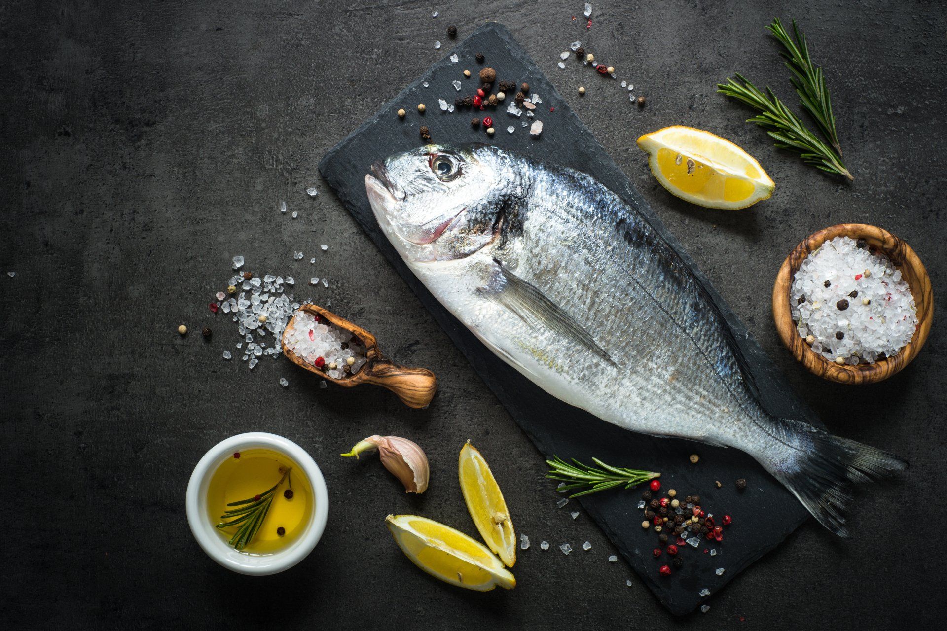 Fresh fish dorado. Dorado and ingredients for cooking at black slate table. Top view with copy space.