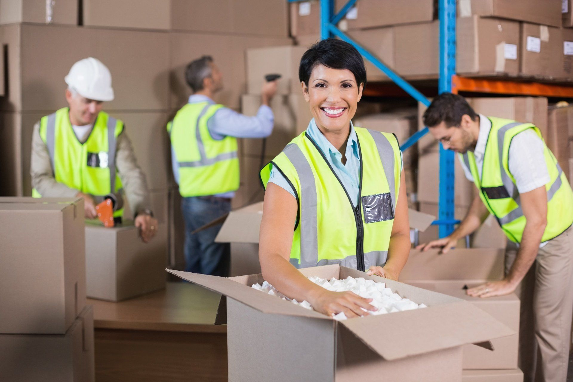 A woman is holding a cardboard box in a warehouse.