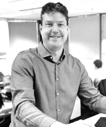 A man in a red shirt is smiling in a black and white photo.