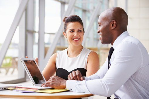 A man and a woman talk over a laptop at an office.