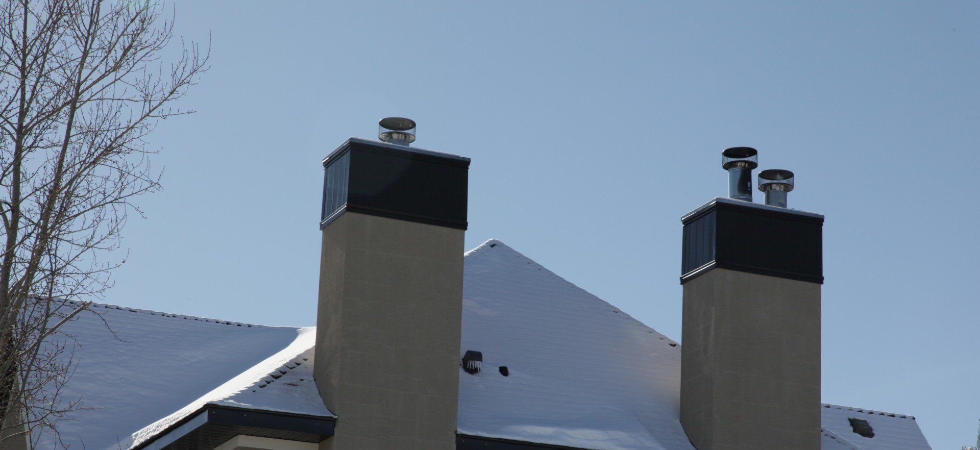 two chimneys on top of a building with snow on the roof