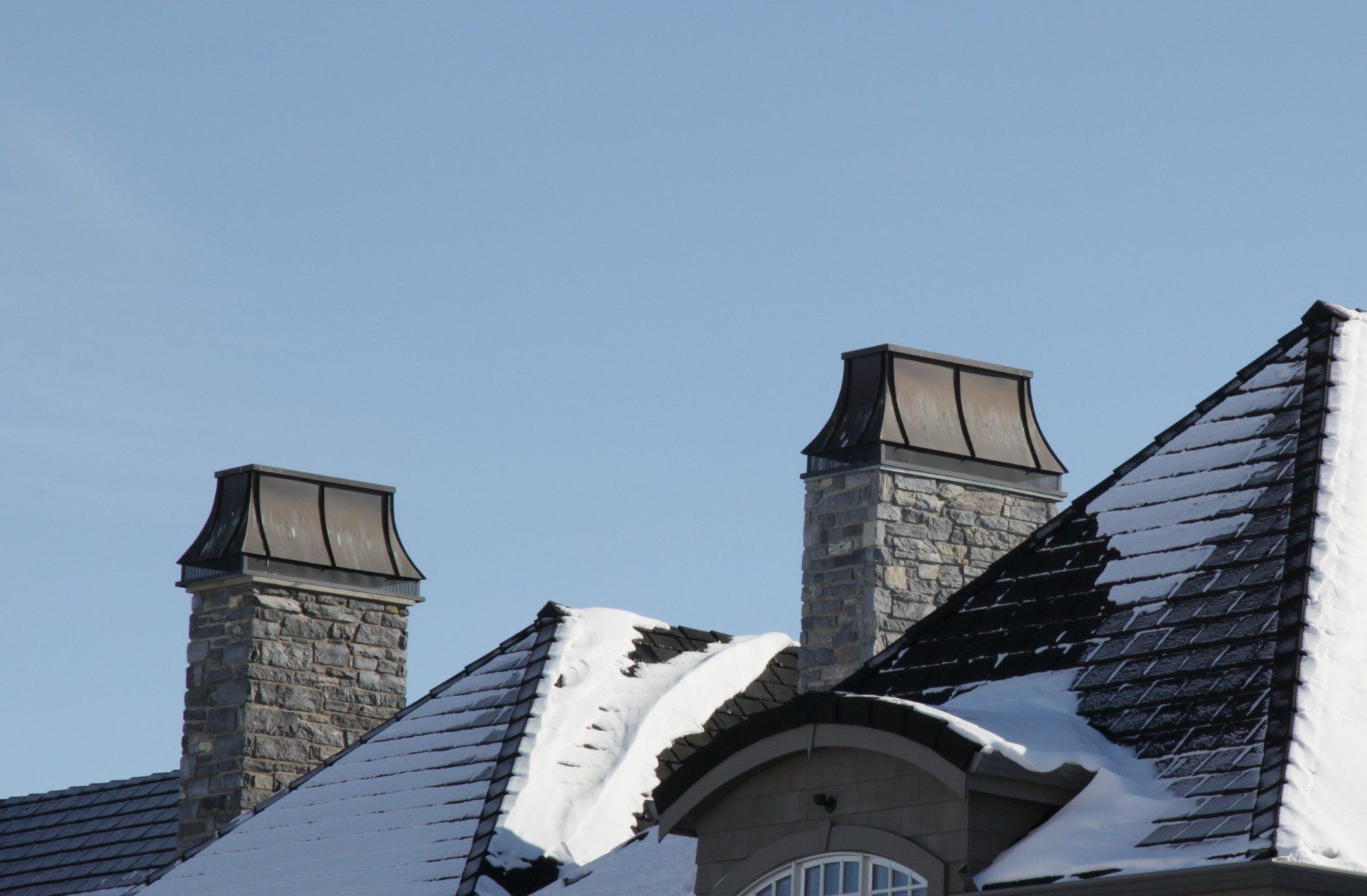 two chimneys on the roof of a house with snow on them