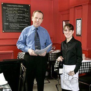 a man and a woman are standing in a restaurant with a menu on the wall behind them