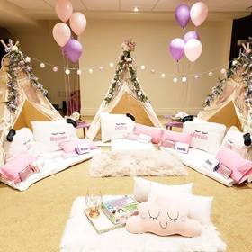 A room decorated for a sleepover with tents , pillows , balloons and flowers.