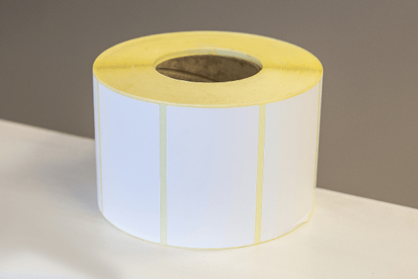 A roll of plain white labels laid on its side on the edge of a white table