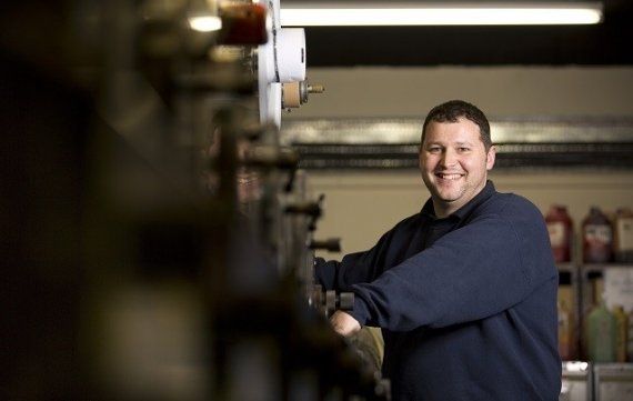 Richard. Secura Labels Production Manager stood next to a press in the factory, looking directly at the camera and smiling
