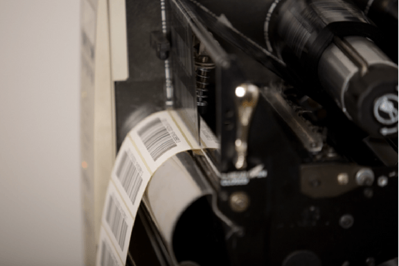 A reel of printed barcode labels appearing from the back of the machine