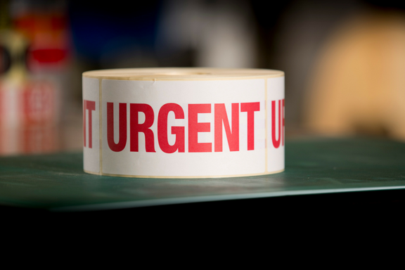 A reel of labels laid on its side on a bench with the word URGENT written in red