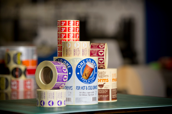 Several rolls of different designs of beautifully printed UV Varnished labels stacked on top of each other on a work bench
