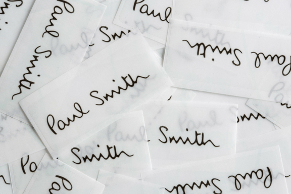Lots of white semi-transparent labels with the Paul Smith signature on, all jumbled up on a flat surface