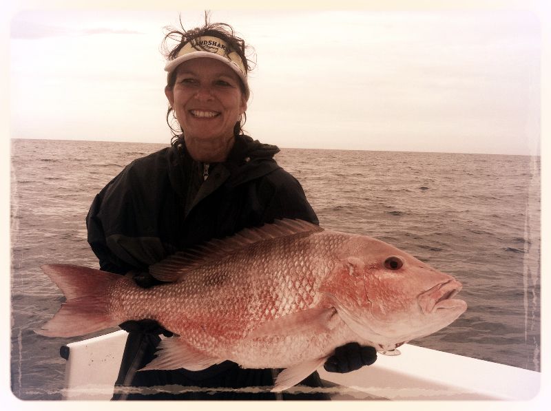 Woman smiling, holding a large red snapper fish on a boat, against a cloudy sky.