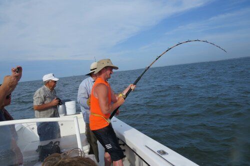 Man fishing on a boat, holding a bent fishing rod. Ocean setting, bright sunny day.