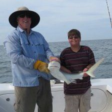 Man and boy on a boat hold a fish. Man in hat, boy in striped shirt, ocean background.