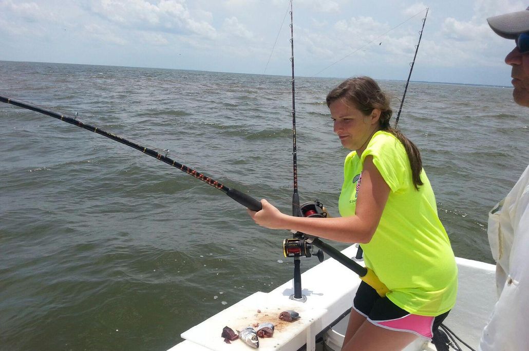 Girl in bright shirt fishing on boat; ocean in background.