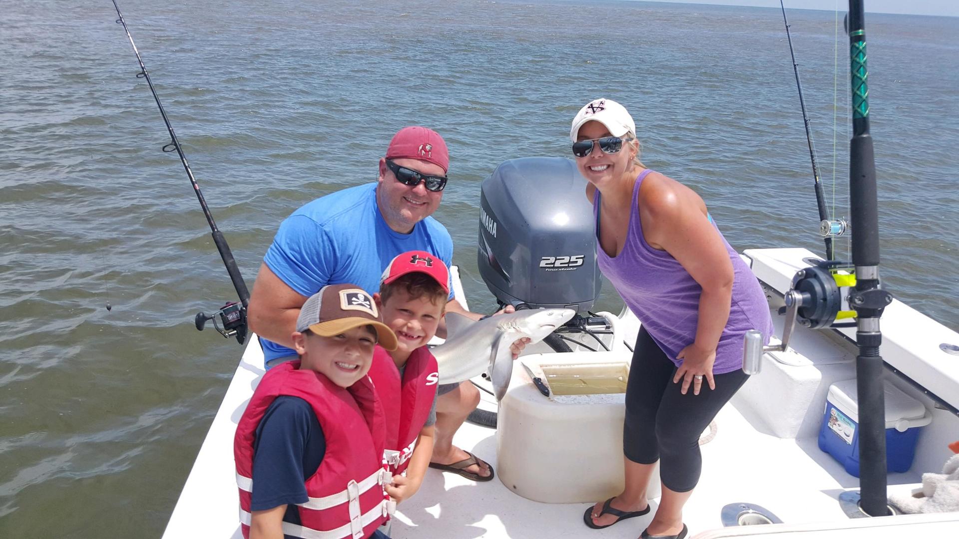 Family on a boat fishing: Man, woman, two children, blue water, sunny day, life vests.