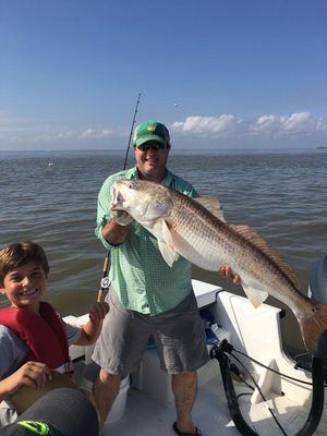 Captain Terry-Shark Man holding large redfish on boat, boy smiling in life vest; water, blue sky.