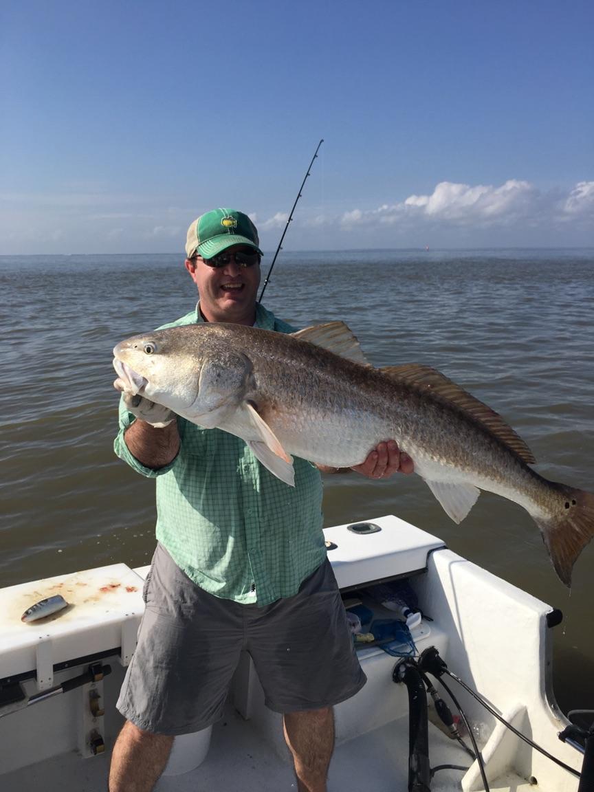 Man holding a large redfish on a boat, green and blue water, sunny day.