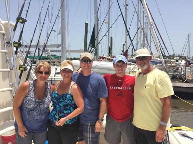 Five people posing on a boat, masts behind them.