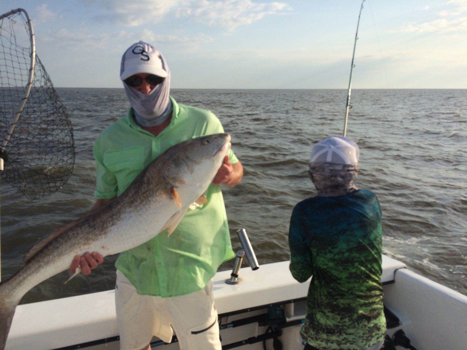 Man holding a large redfish on a boat with another person, near the water.