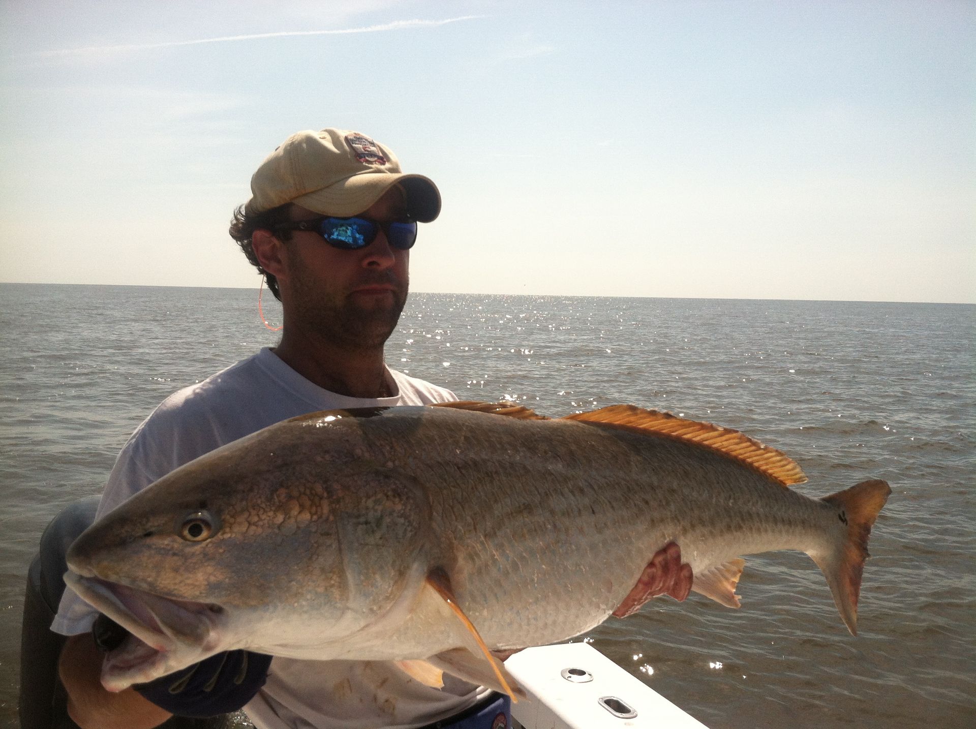Man holding large redfish on a boat, bright sunlight on water.