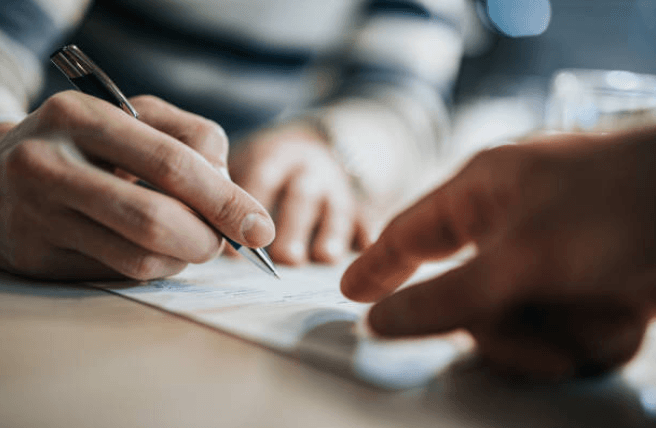 A person is writing on a piece of paper with a pen.